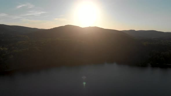 Slow aerial flight over a canadian lake in quebec which is surrounded by trees at sunrise with the s