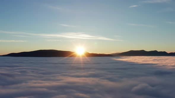 Dramatic sunrise in mountains with low clouds covering valley from aerial view