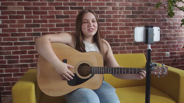 Girl Plays Guitar and Conducts Online Lesson Using Phone on Tripod