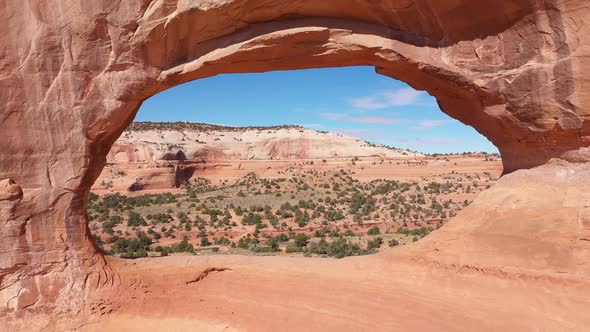 Drone Flies Through Red Orange Stone Arch With Massive Rock Formations In Utah