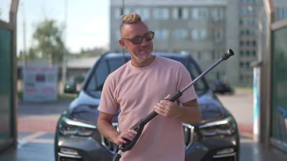 Portrait of Satisfied Caucasian Man Posing with High Pressure Washer at Clean Vehicle at Car Wash