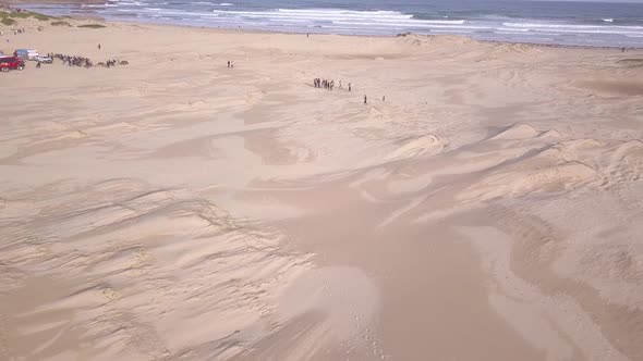 Aerial pull back reveals a wide sandy Stockton Beach next to a sand dunes desert at Port Stephens, S