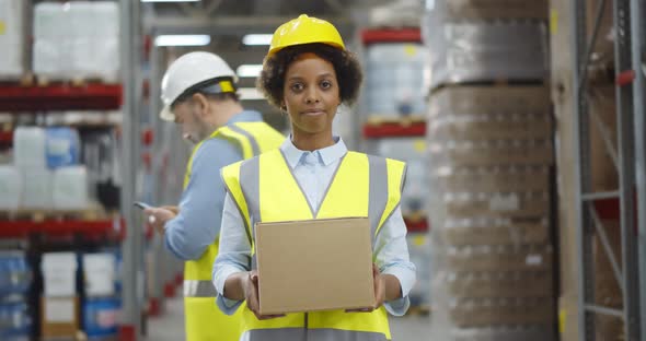 Afroamerican Female Warehouse Worker with Large Box Posing at Camera