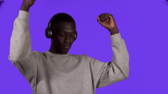 Pleased African Man in White Shirt and Headphones Dancing Relaxfuly with Eyes Closed Over Blue