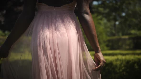 Woman in a pink dress spinning around in a park in slow motion.