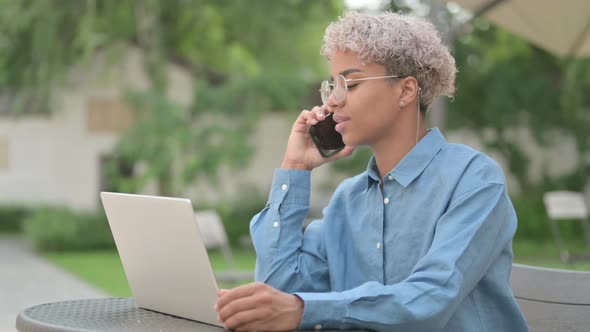 Young African Woman Talking on Phone in Outdoor Cafe