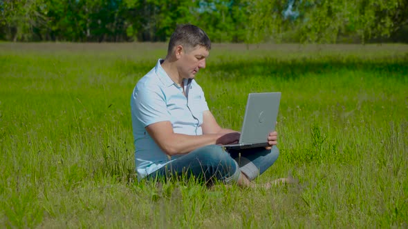 Businessman Works Behind a Laptop Sitting on the Grass