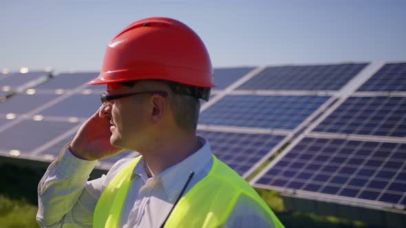 Portrait of Engineer Walks Along the Solar Panels Talking on the Phone