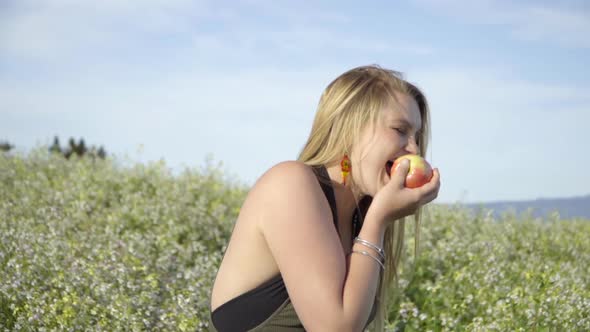 SLOMO of Young Woman Eating an Apple in a Field of Flowers