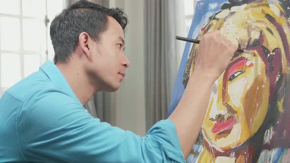 Asian Artist Man Holding Paintbrush And Thinking Before Painting A Girl's Face On The Canvas