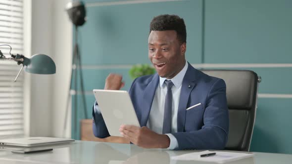 African Businessman Celebrating Success on Tablet in Office