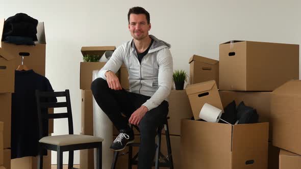 A Happy Moving Man Sits on a Chair and Smiles at the Camera in an Empty Apartment