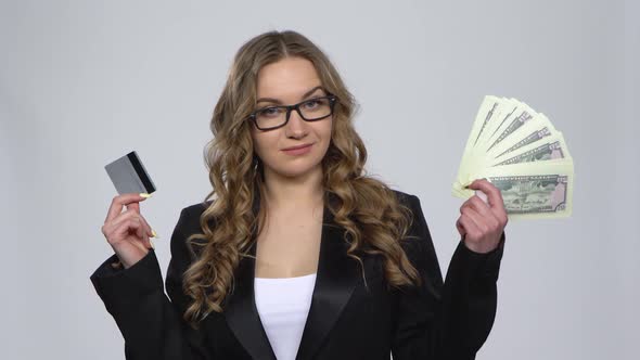 Woman Holds Credit Card and Takes Cash Choosing Between Them Nods Approvingly at Dollar Banknotes