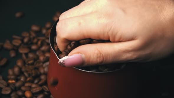 Female Hand Scatters Roasted Coffee Beans with a Cezve