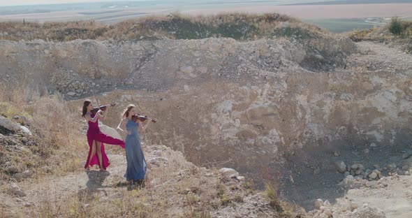 Violinists in Blowing Dresses Play Music Among the Picturesque Cliffs in Summer