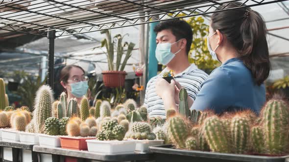 Three asian people with masks on talk about the plants around them in a nursery. Cacti plants are in