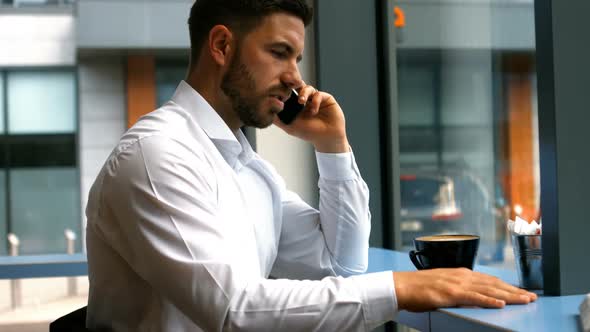 Businessman talking on mobile phone while having coffee