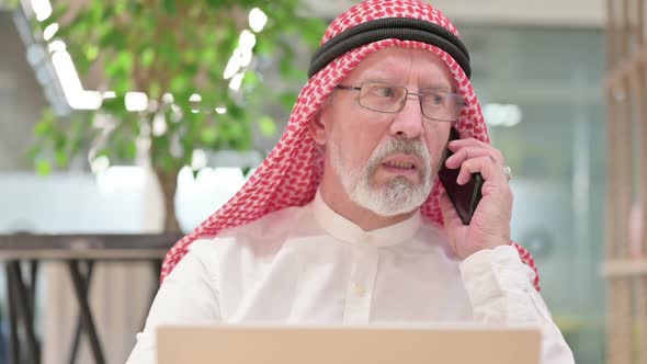 Old Arab Businessman with Laptop Talking on Smartphone