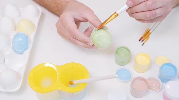 A Man Painting an Egg with Easter Eggs on a White Background Top View