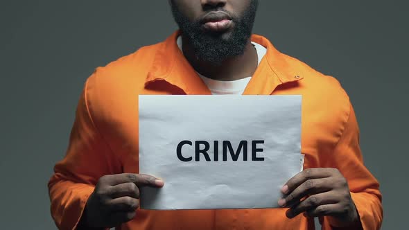 Crime Word on Cardboard in Hands of Black Prisoner, Unlawful Act Punishment