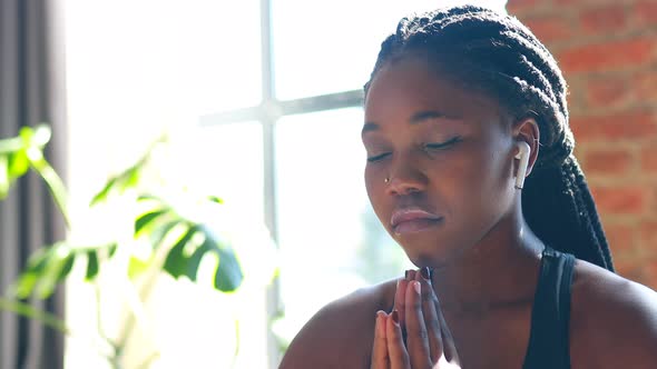 African American Woman in Black Sporty Bra is Sitting Lotus Pose on Yoga Mat Floor Closed Eyes and