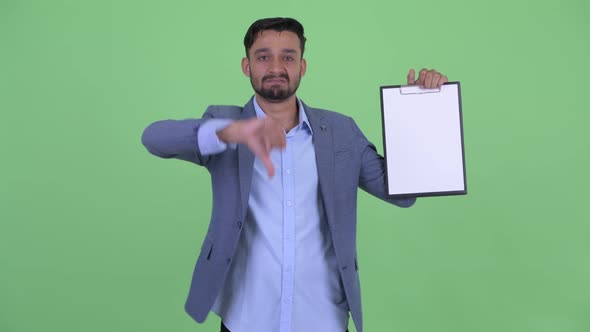 Serious Young Bearded Persian Businessman Showing Clipboard and Giving Thumbs Down