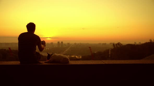 A Man with a Dog Makes a Photo of the Sunrise