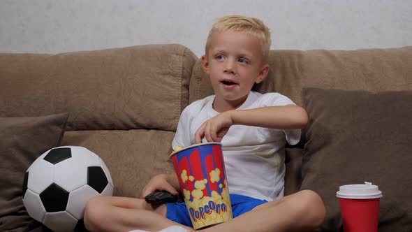 Portrait of a Little Boy on a Sofa with a Remote Control and a Soccer Ball.