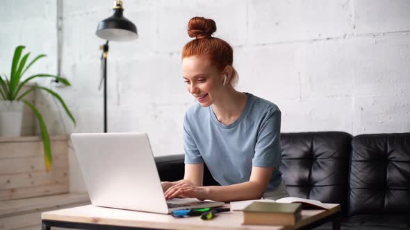 Cheerful Redhead Young Business Woman Is Working on Laptop Computer at Home Office.