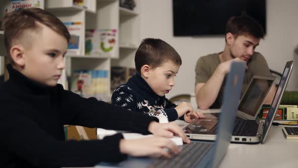 Two Little Boys Typing Something on Laptop Keyboards While Their Male Programmer Teacher is Sitting