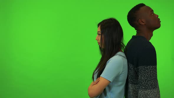 A Young Asian Woman and a Young Black Man Stand with Their Back Against Each Other - Green Screen