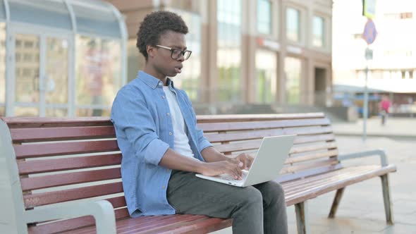 Young African Man with Headache Using Laptop While Sitting Outdoor on Bench