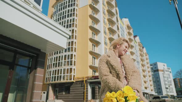 A Happy Girl Walking with a Bouquet of Yellow Tulips Along the Street