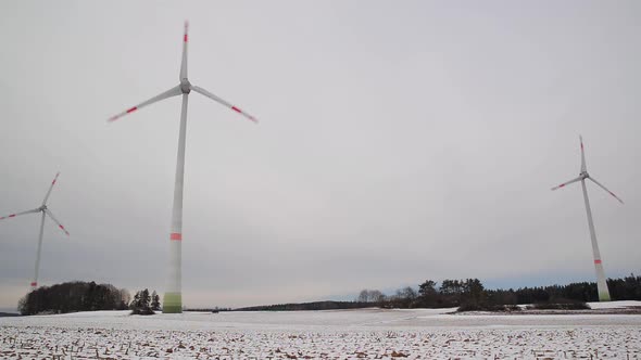 Low angle shot of rotating wind turbines on a snowy field in Germany. Wide shot of a wind farm.