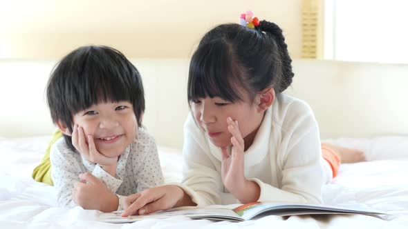 Cute Asian Children Reading A Book On White Bed