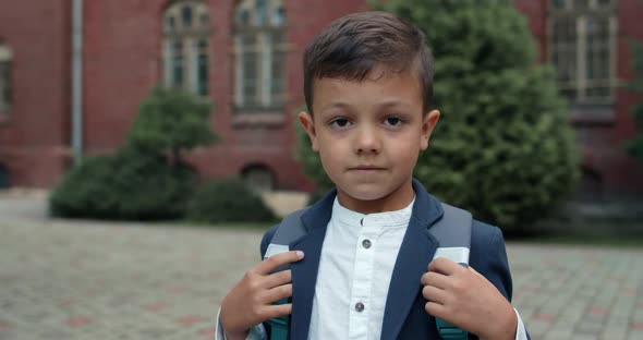 Close Up View of Little Kid with Bag Looking To Camera. Cute Boy in School Uniform Posing While