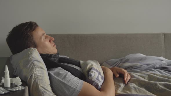 Sick Man Is Lying in His Bed and Blowing His Nose in a Handkerchief