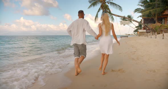 Two Young People in White Clothes Running Along Ocean Tropical Beach Enjoying Romantic Time Together
