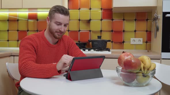 A man watching a video on a tablet while sitting at the kitchen table