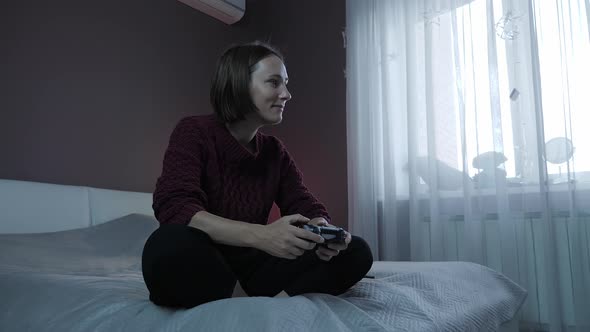 Excited young girl sitting on couch, playing in video games with joystick