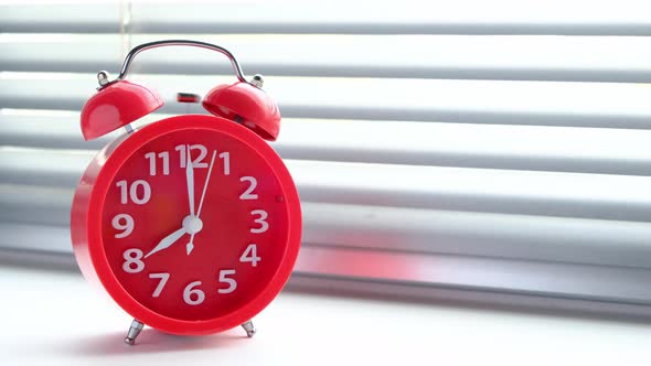 Red alarm clock rang early morning eight clock morning, against background of closed blinds.