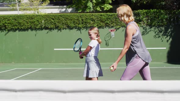 Caucasian mother teaching her daughter to play tennis at tennis court on a bright sunny day