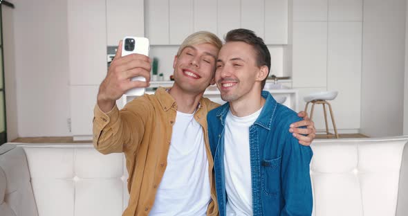 Homosexual Couple Hugging Looking at Smartphone Camera When Making Selfie Photos