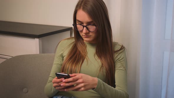 Portrait of Young Woman in Glasses Coughs While Using Phone for Online Shopping in Social Media Sit