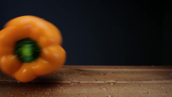 Yellow bell pepper with small water drops falls on board