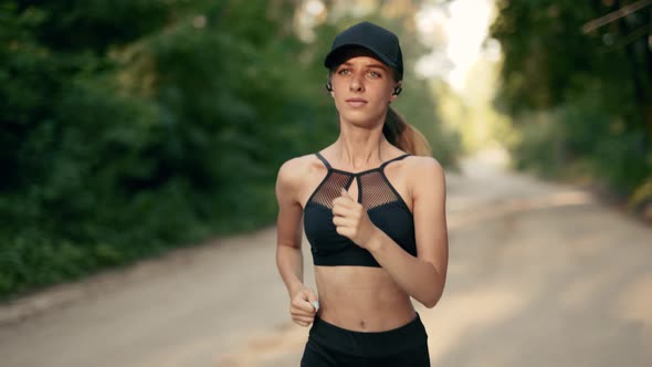A Young Woman Runner is Listening to Music in Earphones and Training in Summer Forest