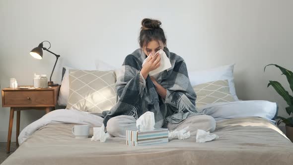 Sick Young Woman with Fever Blows Her Nose in a Napkin Covered in Blanket Having Flu Symptoms