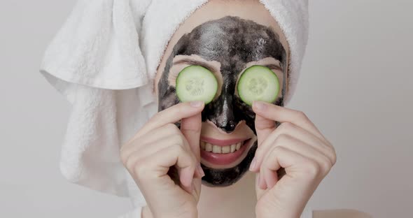 Woman with Black Purifying Charcoal Facial Mask Holding Cucumber Slices Covering Her Eyes