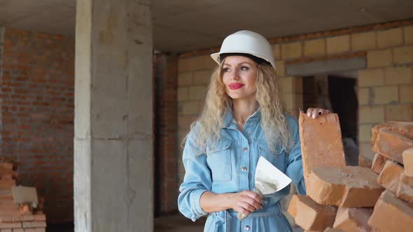 Beautiful Woman Bricklayer with Makeup and Manicure Holding a Brick and a Spatula on the