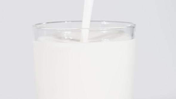 Close up pouring fresh milk in glass over white